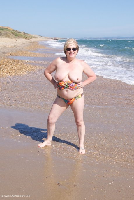 Mature UK woman Speedy Bee wears sunglasses while getting naked at the beach