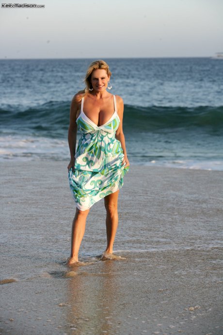 Blonde woman Kelly Madison takes a walk on the beach to reveal her curves
