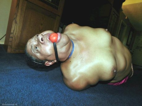 Overweight black woman Trixie struggles against a ball gag while hogtied