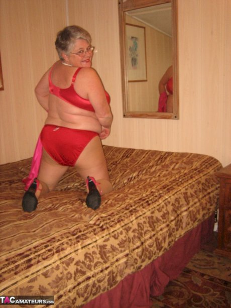 Silver haired nan Girdle Goddess pulls her hose down around her knees on a bed