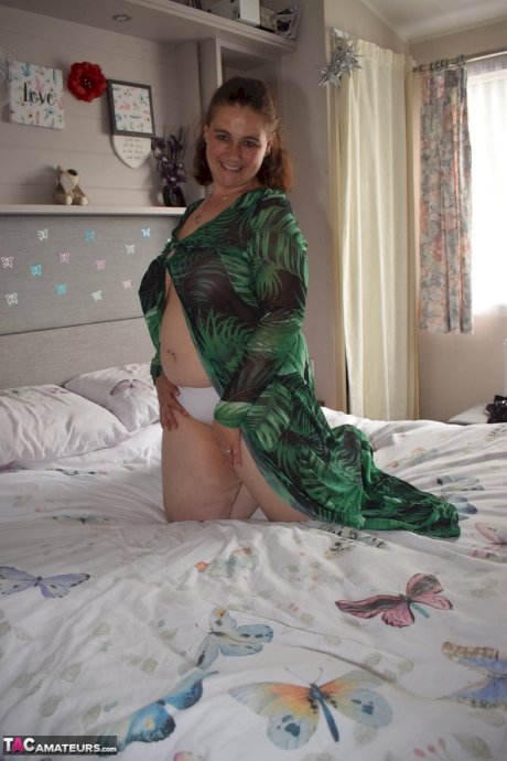 Fat woman exposes herself on a bed while wearing a long dress