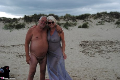 Older platinum blonde Dimonty blows a kiss while at a nude beach with her man