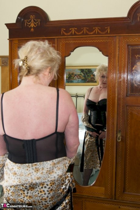 Blonde granny admires herself in a mirror while wearing lingerie and nylons