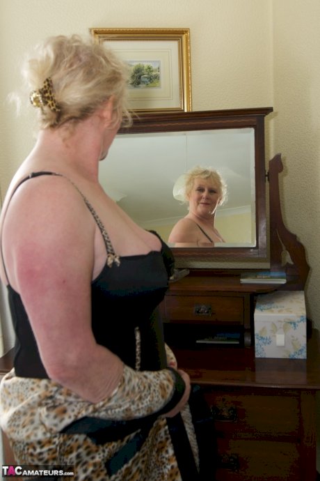 Blonde granny admires herself in a mirror while wearing lingerie and nylons