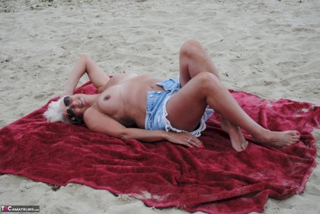 Older platinum blonde Dimonty blows a kiss while at a nude beach with her man