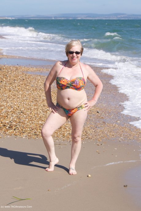 Mature UK woman Speedy Bee wears sunglasses while getting naked at the beach