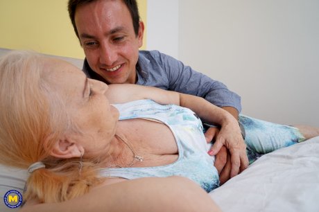 Blonde granny kisses her toy boy after they fuck on top of a bed