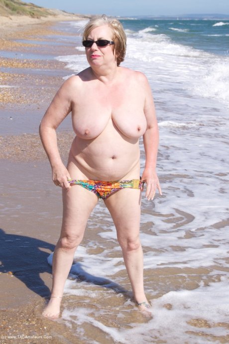 Mature UK woman Speedy Bee wears sunglasses while getting naked at the beach