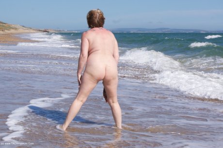 Mature UK woman Speedy Bee wears sunglasses while getting naked at the beach