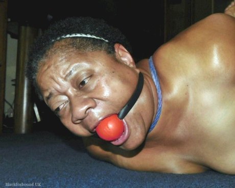 Overweight black woman Trixie struggles against a ball gag while hogtied