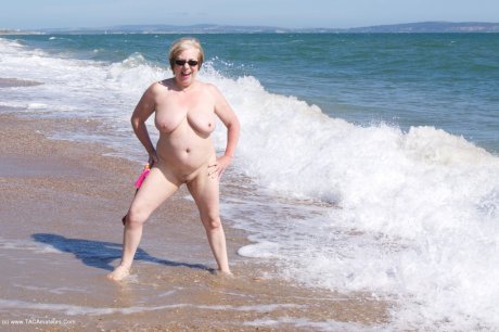 Mature UK woman Speedy Bee wears sunglasses while getting naked at the beach