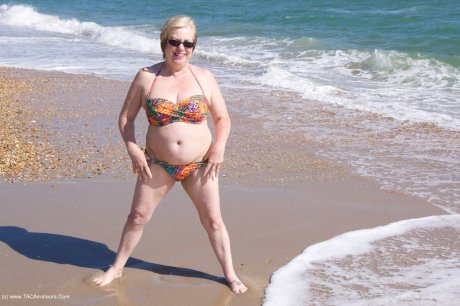 Mature UK woman Speedy Bee wears sunglasses while getting naked at the beach