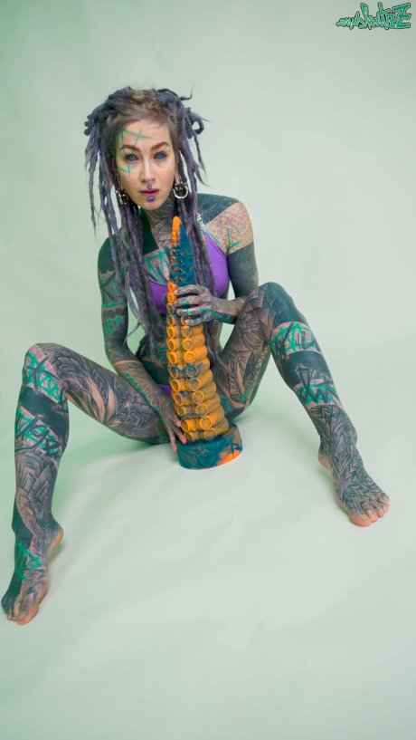 Heavily tattooed girl Anuskatzz holds a couple of taintacle toys in the nude
