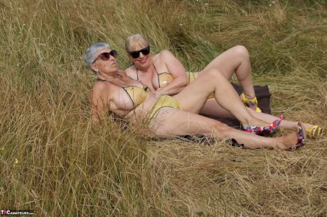 Old lesbians catch rays on their large breasts while sunbathing in a field