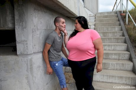 Buxom granny shows her cleavage and sucks a knob on an outdoor stairway