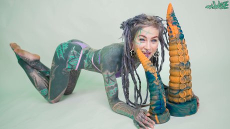 Heavily tattooed girl Anuskatzz holds a couple of taintacle toys in the nude