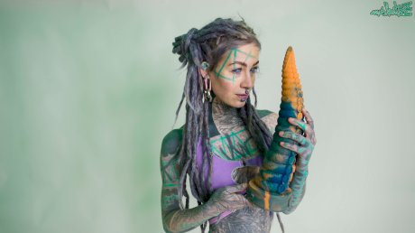 Heavily tattooed girl Anuskatzz holds a couple of taintacle toys in the nude