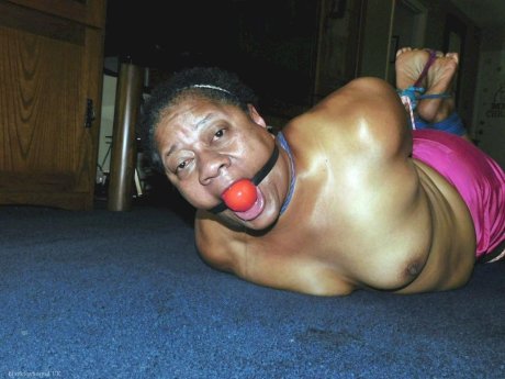 Overweight black woman Trixie struggles against a ball gag while hogtied