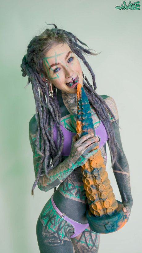 Heavily tattooed girl Anuskatzz holds a couple of taintacle toys in the nude