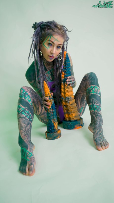 Heavily tattooed girl Anuskatzz holds a couple of taintacle toys in the nude