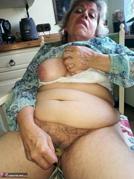 Horny granny Caro sticks a banana inside her natural pussy on kitchen chair