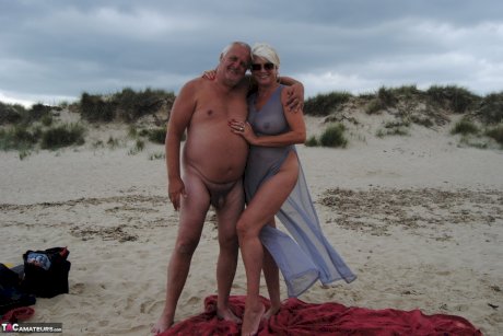 Older platinum blonde Dimonty blows a kiss while at a nude beach with her man