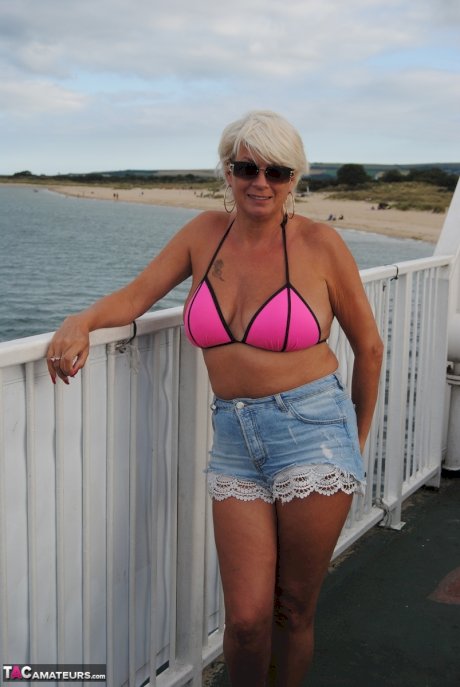 Older platinum blonde Dimonty blows a kiss while at a nude beach with her man