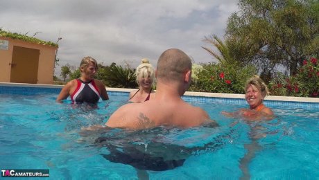 Older blond Sweet Susi and a girlfriend jerk a guy's dick underwater in a pool