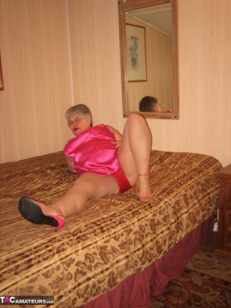 Silver haired nan Girdle Goddess pulls her hose down around her knees on a bed