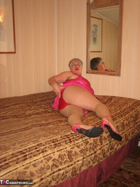 Silver haired nan Girdle Goddess pulls her hose down around her knees on a bed