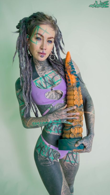 Heavily tattooed girl Anuskatzz holds a couple of taintacle toys in the nude