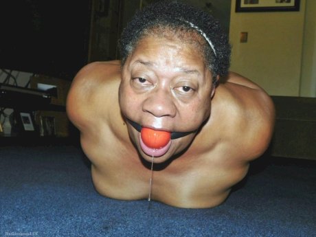 Overweight black woman Trixie struggles against a ball gag while hogtied