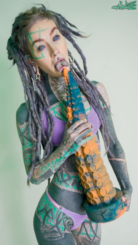 Heavily tattooed girl Anuskatzz holds a couple of taintacle toys in the nude