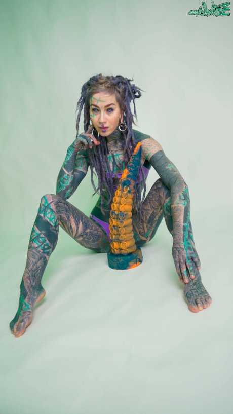 Heavily tattooed girl Anuskatzz holds a couple of taintacle toys in the nude