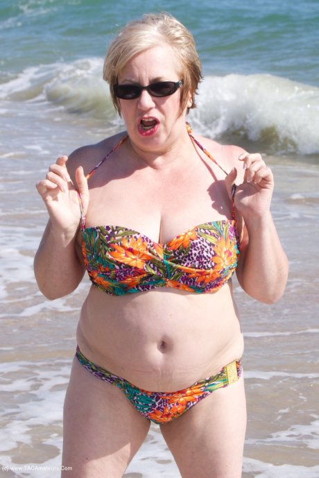 Mature UK woman Speedy Bee wears sunglasses while getting naked at the beach