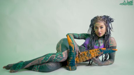 Heavily tattooed girl Anuskatzz holds a couple of taintacle toys in the nude